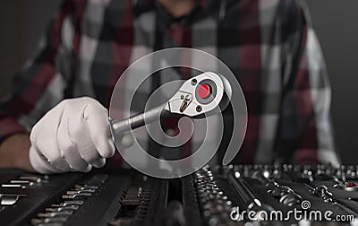 Hand in glove closeup with metal steel socket ratchet handle over toolkit Stock Photo