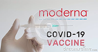 Hand with glove holds syringe next to Moderna logo, one of the companies developing a Covid-19 Coronavirus vaccine. Editorial Stock Photo