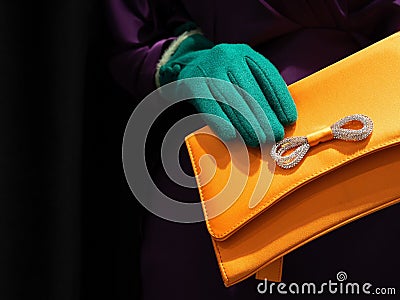 Hand with a green glove holding a bright yellow clutch bag Editorial Stock Photo