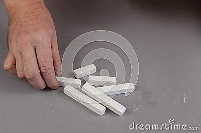 The hand of a grown man takes a piece of chalk lying on a gray b Stock Photo