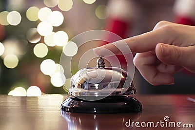 Hand of guest ringing reception bell on desk of guesthouse, hotel at christmas time. Color shining garland on christmas tree Stock Photo