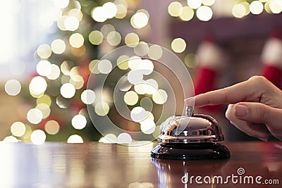 Hand of guest ringing reception bell on desk of guesthouse, hotel at christmas time. Color shining garland on christmas tree Stock Photo