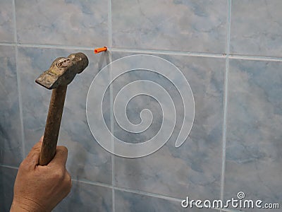 A hand with a hammer drives a dowel into the wall Stock Photo