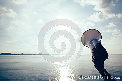 Hand hold megaphone against sea under sky Stock Photo