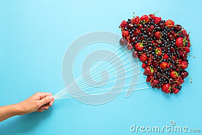 Hand holding balloons made of berries on blue paper background. Healthy eating concept. Flat lay Stock Photo
