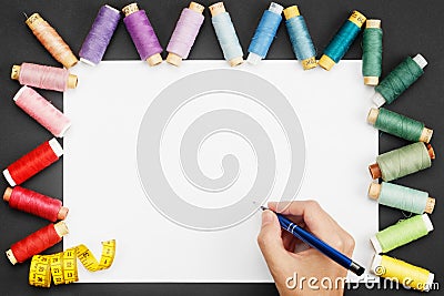 Hand holding a ballpoint pen over a white sheet of paper with colored threads coils and a tailor meter Stock Photo