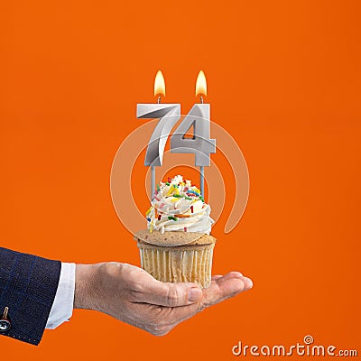 Hand holding birthday cupcake with number 74 candle - background orange Stock Photo