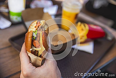 A hand is holding bitten hamburger. Tray with food on the background Stock Photo
