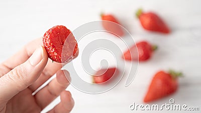 Hand holding bitten strawberry on white wooden background. Summer berry pleasure. Scattered strawberries Stock Photo