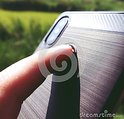 The hand is holding a black phone and the index finger is touching the fingerprint scanner to unlock the smartphone Stock Photo