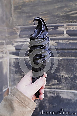 Hand holding black soft serve ice cream cone made with activated charcoal Stock Photo