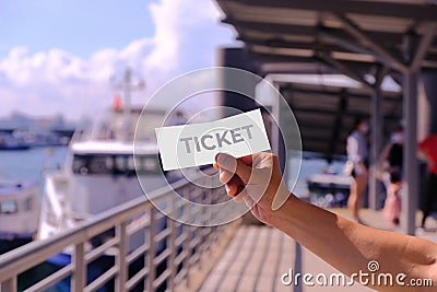 Hand holding blank mockup for one-fold ticket design, at a pier. Cruise ferry and incidental people in the background, defocused. Stock Photo