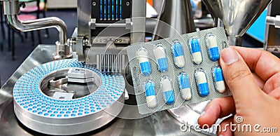 Hand holding blue capsule pack at medicine pill production line Stock Photo