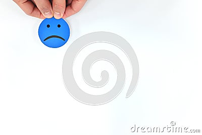 Hand holding a blue sad emoticon in white background with copy space. Unsatisfied client and bad customer service concept. Stock Photo