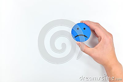 Hand holding a blue sad face in white background with copy space. Sadness and bad customer service concept. Stock Photo