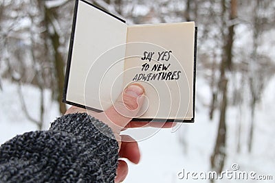 Hand holding a book with the inscription Say yes to new adventures on the background of the winter forest Stock Photo