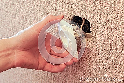 Hand holding a broken outlet, risking electric shock Stock Photo