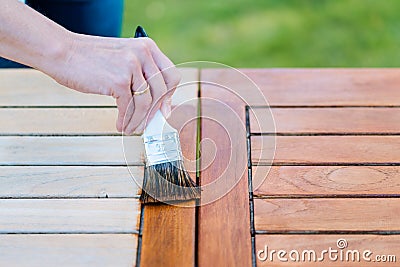Hand holding a brush applying varnish paint on a wooden garden table - painting and caring for wood Stock Photo