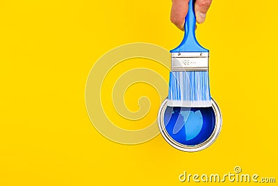 Hand holding Brush on open can of paint on yellow background. Renovation concept - Image Stock Photo