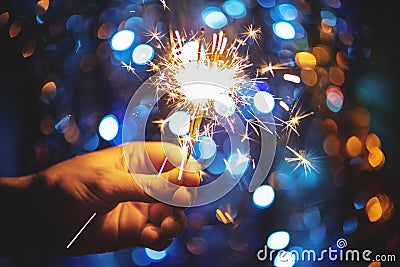 Hand holding a burning sparkler firework on Christmas light bokeh background. Stock Photo