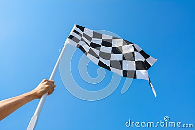 Hand holding checkered flag on blue sky background Stock Photo