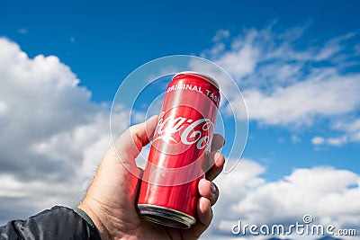 Hand holding a Coca Cola can towards bright blue and cloudy sky outdoors Editorial Stock Photo