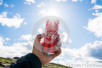 Hand holding a Coca Cola can towards bright blue sky Editorial Stock Photo