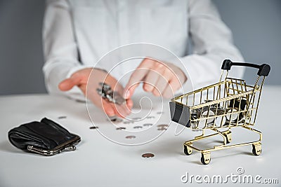 Hand holding a coin with pile of coin in the shopping cart on white and grey background Stock Photo