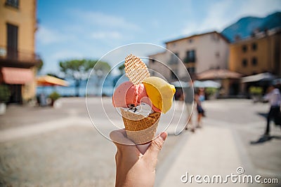 Hand holding cone with colorful delicious italian gelato ice-cream in Menaggio town near Como lake Stock Photo