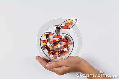 Hand holding drawing apple with colorful capsules and pills on white background. Health care vitamins or synthetic food concept. Stock Photo