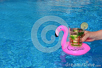 Hand holding a drink in an inflatable pink flamingo drinks holder in swimming pool Stock Photo