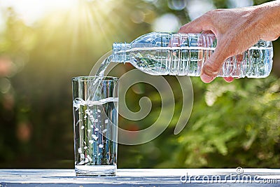 Hand holding drinking water bottle pouring water into glass on wooden table Stock Photo