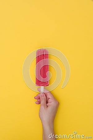 Hand holding a fresh strawberry popsicle on yellow background Stock Photo