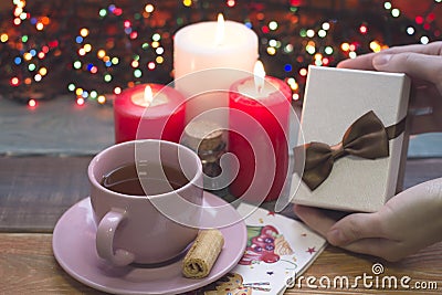 Hand holding a a gift box, a cup of tea, burning candles Stock Photo