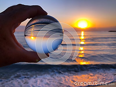 Hand holding glass ball, beach to sea view at dawn Stock Photo