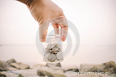 Hand holding glass jar contain with coin at the beach Stock Photo