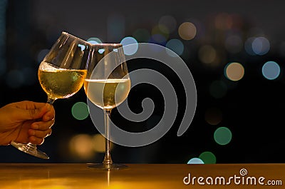 Hand holding a glass of white wine toasting to celebration and party concept put on wooden table of rooftop bar with colorful Stock Photo
