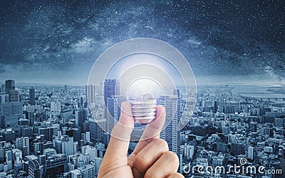 Hand holding glowing light bulb, with futuristic city background Stock Photo