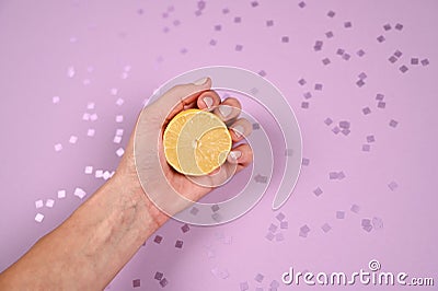 Hand holding half lemon on violet spa barkles ckground. Woman's handwith a piece of lemon. Top view, copy space Stock Photo