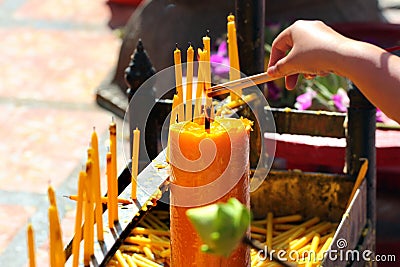 Hand holding incense sticks, lighting from the burning yellow candle. Traditional Thailand buddhist concept Stock Photo