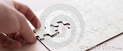 a hand holding a jigsaw piece and complete puzzle on the table Stock Photo