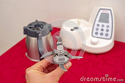 hand holding kitchen robot blade with respective machine in background. Stock Photo