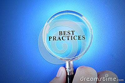 Hand holding magnify glass over a blue background with BEST PRACTICES words. Stock Photo