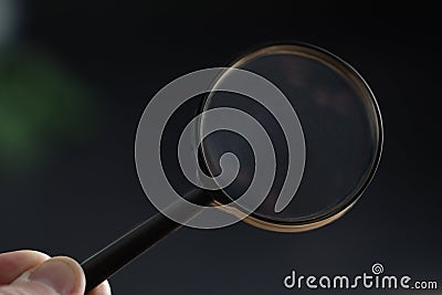 hand holding magnifying glass in dark room. concept of uncovering mystery, detective investigation, solve secret Stock Photo