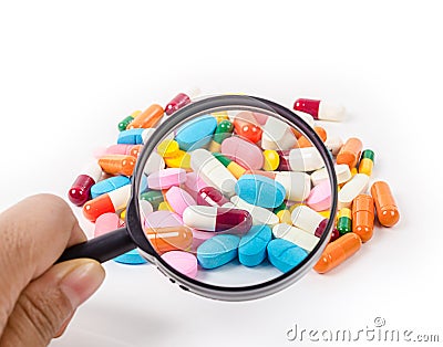 Hand holding magnifying glass with medicine pills. Stock Photo