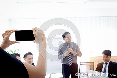 Hand holding mobile phone for taking photo or VDO of business discussing conference with blurred background of brainstorming Stock Photo