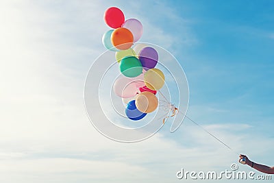 Hand holding multicoloured balloons for relax on tropical beach sunny day, vintage tone. Stock Photo