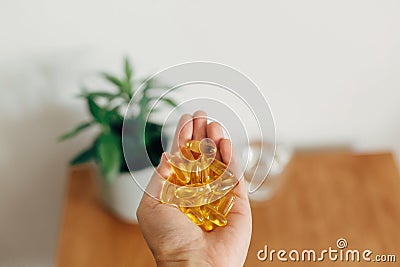 Hand holding omega 3 capsules above wooden table with glass of water. Morning dose of vitamin. Fish oil in pills. Health support Stock Photo