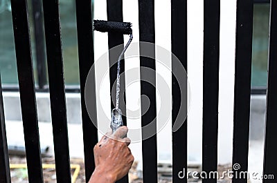 Hand holding paint roller applying black paint on the fence Stock Photo