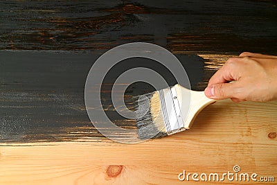 Hand holding paintbrush painting the surface of wooden furniture with dark grey paint Stock Photo